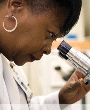 Female in lab coat looking in microscope