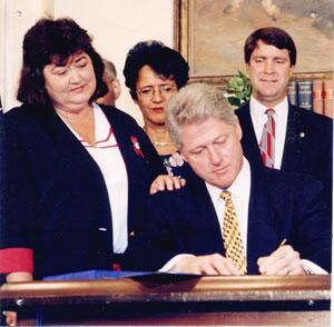 Bill Clinton signing the Ryan White Care Act while White's mother looks on.