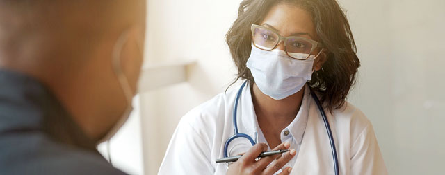 a masked doctor takes notes while talking with a patient